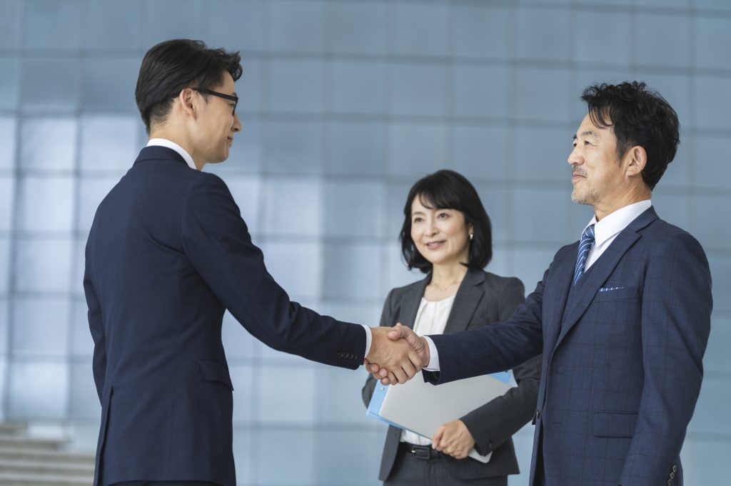 「中国の取引先とメールや商談をする際、相手をどう呼ぶのが正解だろう」と悩んでいませんか。辞書を引くと「客户 kèhù」や「合作伙伴 hézuò huǒbàn」など様々な単語が出てくるため、実務でどれを使うべきか迷うこともあると思います。 中国語のビジネスコミュニケーションでは、相手との関係に合った言葉を選ぶことが、良好な関係づくりにつながります。 本記事では、顧客・パートナー・商社など、状況に応じた「取引先」の中国語表現の使い分けと、仕事で使いやすい実務フレーズを紹介します。 これまで中国企業とやり取りを行っていた経験をもとに、現場で役立つ表現をまとめました。この記事を読めば、取引先とのやり取りで使いやすい表現が分かり、実務で迷いにくくなります。  取引先の中国語表現 日本語では「取引先」と一言で表しますが、中国語では相手との関係によって表現が変わります。 まずは実務でよく使う言葉の違いを確認し、そのまま使えるフレーズも見ていきましょう。  相手の立場によって単語を使い分ける  中国語では、日本語の「取引先」をそのまま一つの単語で表さず、相手との関係によって言葉を使い分けることが一般的です。  中国語 ピンイン 意味 関係性供应商gōngyìngshāng仕入先・サプライヤー部品や材料などを提供する会社客户kèhù顧客・取引先商品やサービスを購入する相手合作伙伴hézuò huǒbàn協力会社・パートナー一緒に仕事やプロジェクトを進める相手 相手との関係に合った表現を使うことは、仕事を円滑に進めることにもつながります。  実務で使えるフレーズ  供应商已经确认交期了。 Gōngyìngshāng yǐjīng quèrèn jiāoqī le. （仕入先より納期確認済みです。） 客户提出了新的要求。 Kèhù tíchū le xīn de yāoqiú. （取引先から新しい要望がありました。） 我们正在寻找新的合作伙伴。 Wǒmen zhèngzài xúnzhǎo xīn de hézuò huǒbàn. （新しい協力先を探しています。） 顧客の中国語表現 日本語の「顧客」や「クライアント」を表す中国語には、いくつかの表現があります。 しかし、企業間取引か一般消費者向けの取引かによって使われる単語が異なるため、実務ではその違いを正しく理解しておくことが重要です。  企業間の取引では「客户 kèhù」が一般的  ビジネスの現場、特に企業間取引で「顧客」や「お客さま」を指す場合は、「客户 kèhù」を使うのが最も一般的です。また、日本語の「顧客」をそのまま漢字にした「顾客 gùkè」という表現もありますが、こちらは店舗や小売店など一般消費者を指す場面で使われることが多いです。   中国語 ピンイン 意味 実務でのニュアンス客户kèhù顧客・クライアント法人間取引で最も広く使われる表現顾客gùkè顧客・お客さま店舗や一般消費者向けで使われる表現甲方jiǎfāng発注側契約書やプロジェクトで立場を表す表現 企業同士のやり取りでは「客户 kèhù」を使う、と覚えておくと便利です。 実務で使えるフレーズ 同じ「顧客」を意味する言葉でも、使う場面によって表現が変わります。  明天我们公司的重要客户要来参观工厂。 Míngtiān wǒmen gōngsī de zhòngyào kèhù yào lái cānguān gōngchǎng. （明日は弊社のVIP顧客が工場見学に来られます。） 本周末商场将举办面向VIP客户的特惠活动。 Běn zhōumò shāngchǎng jiāng jǔbàn miànxiàng VIP kèhù de tèhuì huódòng. （今週末、ショッピングモールではVIP顧客向けの特別セールを開催します。）  パートナーの中国語表現 ビジネスで対等にプロジェクトを進める「パートナー」の表現には、いくつか種類があります。 相手が「企業（法人）」なのか「担当者（個人）」なのかによって、使い分けることがポイントです。   協力して仕事を進める相手なら「合作伙伴 hézuò huǒbàn 」  企業同士で協力して仕事を進める相手には、「合作伙伴 hézuò huǒbàn」を使うことが一般的です。一方、仕事で一緒に活動する同僚や担当者を指す場合は「工作伙伴 gōngzuò huǒbàn」や「搭档 dādàng」を使うことがあります。相手との関係性によって使い分けることがポイントです。   中国語 ピンイン 意味 実務でのニュアンス合作伙伴hézuò huǒbànビジネスパートナー企業間で最も広く使う表現工作伙伴gōngzuò huǒbàn仕事仲間・同僚一緒に働くメンバーを指すことが多い搭档dādàng相棒・ペア個人間で使うことが多い表現 実務で使えるフレーズ  メールや商談の場でそのまま使える表現を例文で紹介します。  贵司是本公司最值得信赖的合作伙伴。 Guìsī shì běn gōngsī zuì zhídé xìnlài de hézuò huǒbàn. （貴社は弊社にとって最も信頼できるパートナーです。） 她是我最信赖的工作伙伴。 Tā shì wǒ zuì xìnlài de gōngzuò huǒbàn. （彼女は私の最も信頼している仕事仲間です。） 関係構築で使える中国語表現 取引先とのやり取りでは、定型挨拶だけでなく感謝や協力姿勢を伝える場面が多くあります。 相手への配慮を言葉にして、良好な関係を築くための実務フレーズを見ていきましょう。 関係を深めるフレーズ集 希望这次能和贵司一起合作。 Xīwàng zhè cì néng hé guìsī yìqǐ hézuò. （今回の案件について御社と一緒に協力していきたいです。） 让我们一起努力解决这个问题。 Ràng wǒmen yìqǐ nǔlì jiějué zhège wèntí. （お互いに協力して、一緒に乗り越えましょう。） 感谢贵司迅速对应 ，真的帮了我们很多。 Gǎnxiè guìsī xùnsù duìyìng, zhēn de bāng le wǒmen hěn duō. （御社が迅速に対応してくれて本当に助かりました。） 这次项目能顺利进行，多亏大家的支持。 Zhè cì xiàngmù néng shùnlì jìnxíng, duōkuī dàjiā de zhīchí. （今回のプロジェクトがうまく進んだのは、皆様のおかげです。） 希望今后继续合作。 Xīwàng jīnhòu jìxù hézuò. （今後も引き続きご協力のほどよろしくお願いいたします。） 一緒に進めていく姿勢や感謝の気持ちを伝えることで、相手との距離が縮まり、やり取りも進めやすくなります。ここぞという場面で使ってみてください。  商社の中国語表現 中国語で、「商社」を指す中国語表現はいくつか存在します。 相手の役割や立場に合わせた適切な言葉遣いと、実務で使える表現を確認していきましょう。  中国語では「贸易公司 màoyì gōngsī」が伝わりやすい  中国語で商社は「贸易公司 màoyì gōngsī」と表現することが一般的です。 また、販売代理店を指す「代理商 dàilǐshāng」や、販売店を表す「经销商 jīngxiāoshāng」という言葉もありますが、まずは「贸易公司  màoyì gōngsī」を覚えておくと実務で使いやすくなります。  実務で使えるフレーズ  取引先がメーカーなのか商社なのかを確認する場面で使うことがあります。 请问贵司是厂家还是贸易公司？ Qǐngwèn guìsī shì chǎngjiā háishi màoyì gōngsī? （貴社はメーカーですか、それとも商社ですか。） 我们正在寻找新的贸易公司合作。 Wǒmen zhèngzài xúnzhǎo xīn de màoyì gōngsī hézuò. （新しい商社との協力先を探しています。） まとめ 今回は、中国語で使う取引先の表現についてまとめました。 取引先は一つの言葉で表すのではなく、顧客・協力会社・商社など相手との関係によって表現が変わります。 今日紹介した表現の中から、まずは1つ実際の仕事で使ってみてください。今後、取引先とのやり取りをスムーズに進める第一歩になるはずです。