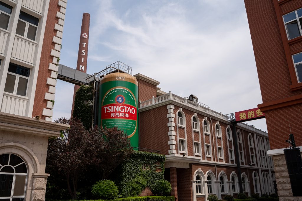 Front view of a brick building with a large Tsingtao beer can sign against a blue sky.
